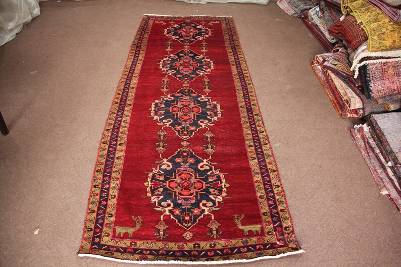 K&ouml;nnte beinhalten: Ein langer roter L&auml;uferteppich mit traditionellem persischem Design. Der Teppich hat eine dunkelblaue Mitte mit komplizierten Blumenmustern und einen gold-schwarzen Rand.