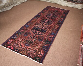 Könnte beinhalten: Ein langer, schmaler Teppich mit traditionellem persischem Design. Der Teppich hat einen dunkelblauen Rand mit komplizierten Mustern in Rosa-, Rot- und Blautönen.