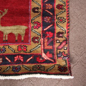 K&ouml;nnte beinhalten: Ein roter Teppich mit einem braunen und blauen Rand. Der Teppich hat ein stilisiertes Hirsch-Design in der Mitte. Der Teppich hat einen Fransenrand.