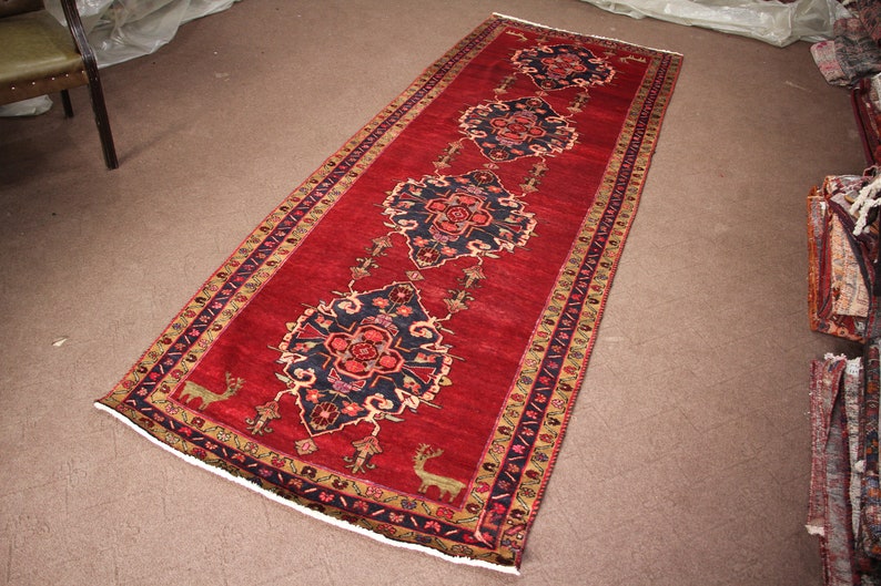 K&ouml;nnte beinhalten: Ein roter L&auml;ufer mit traditionellem persischem Design. Der Teppich hat eine dunkelblaue Mitte mit einem Blumenmuster und einen roten Rand mit einem geometrischen Muster.