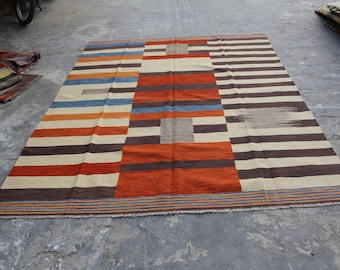 May include: A striped rug with a geometric pattern in shades of brown, orange, blue, and white. The rug has a fringe border.