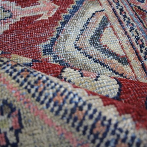 May include: Close-up of a red, blue, and beige patterned rug with a woven texture. The rug is folded in half, showing the intricate details of the design.