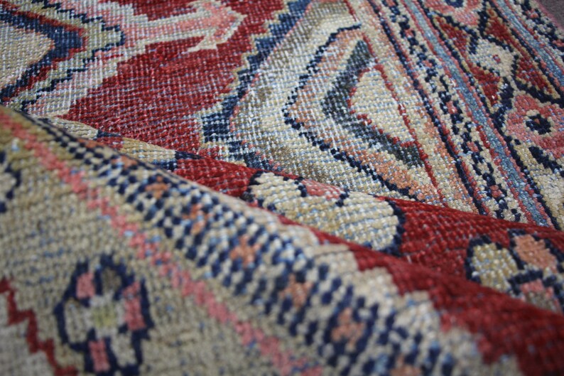 May include: Close-up of a red, blue, and beige patterned rug with a woven texture. The rug is folded in half, showing the intricate details of the design.