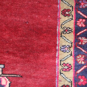 K&ouml;nnte beinhalten: Ein roter Teppich mit einem gemusterten Rand. Der Rand zeigt ein sich wiederholendes Muster aus Blumen und Bl&auml;ttern in den Farben Rosa, Blau und Gr&uuml;n.