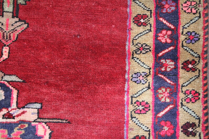 K&ouml;nnte beinhalten: Ein roter Teppich mit einem gemusterten Rand. Der Rand zeigt ein sich wiederholendes Muster aus Blumen und Bl&auml;ttern in den Farben Rosa, Blau und Gr&uuml;n.