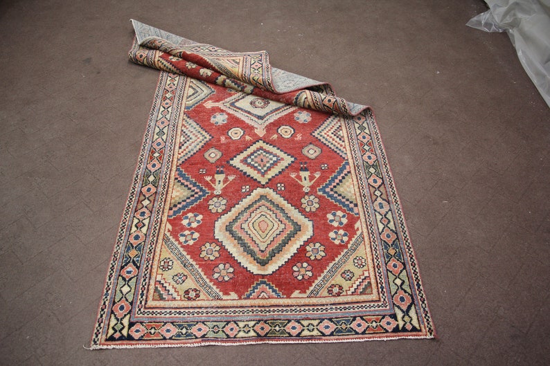 May include: A red, beige, and blue patterned rug with a geometric design. The rug has a fringe border.