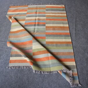 May include: A multi-colored striped rug with a fringe border. The rug is folded in half and the colors are orange, blue, green, and beige.