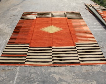 May include: A large, rectangular rug with a geometric pattern. The rug has a central diamond shape in a light yellow color, surrounded by a red border. The rest of the rug is a combination of black and white stripes.