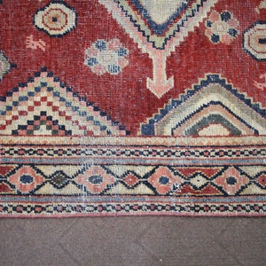 May include: A red, blue, and cream colored rug with a geometric pattern. The rug has a fringe border.