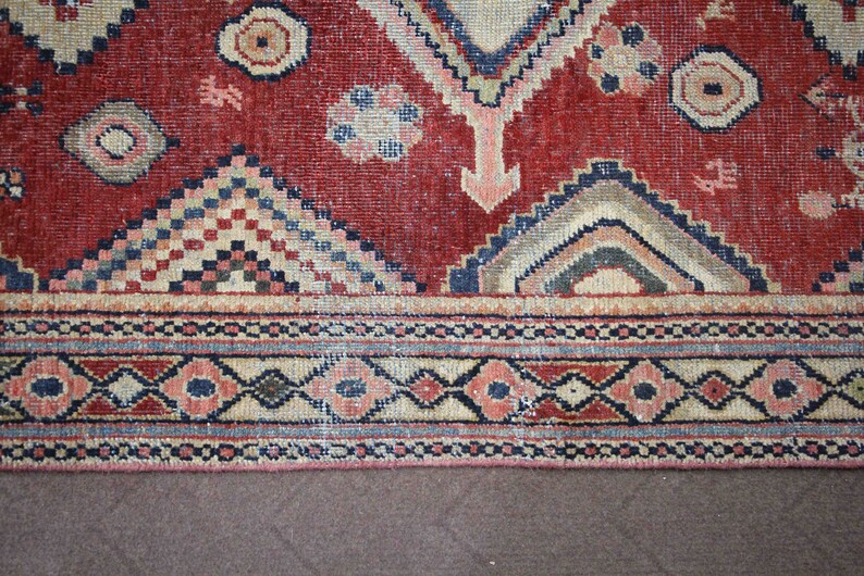 May include: A red, blue, and cream colored rug with a geometric pattern. The rug has a fringe border.