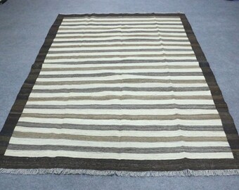 May include: A striped rug with a brown border and fringe. The rug has a cream background with brown and gray stripes.