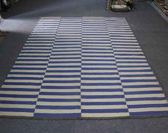 May include: A blue and white striped rug with a fringe border. The rug is made of a woven material and has a simple, geometric design.