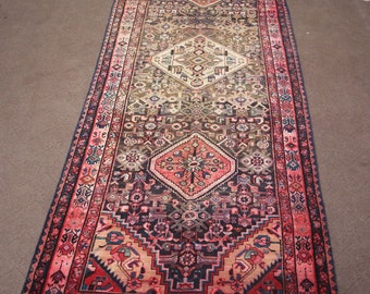 Könnte beinhalten: Ein langer, schmaler Teppich mit traditionellem persischem Design. Der Teppich hat einen dunkelblauen Rand mit komplizierten Mustern in Rot-, Rosa- und Cremetönen. Die Mitte des Teppichs zeigt ein großes, rautenförmiges Medaillon mit einem floralen Motiv.