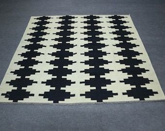 Puede incluir: Alfombra geométrica con estampado en blanco y negro sobre fondo crema. La alfombra tiene un borde de flecos.