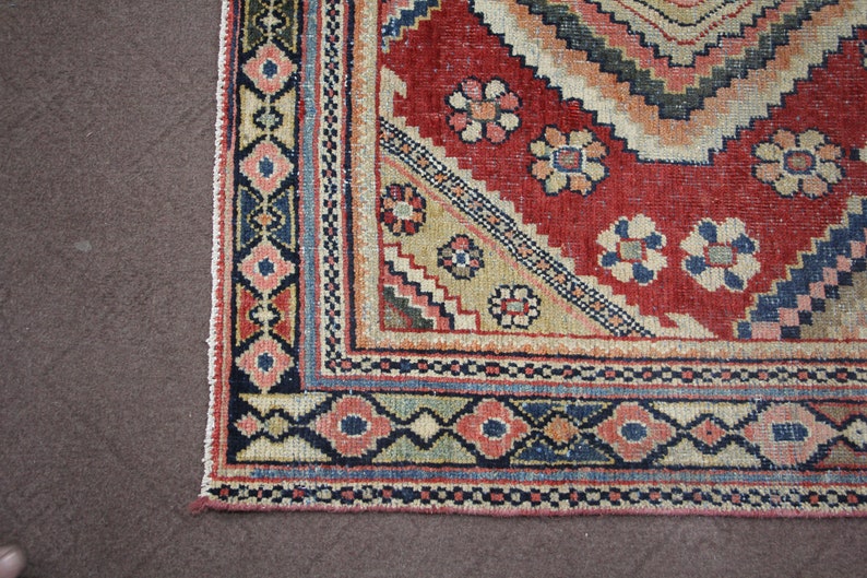 May include: Close-up of the bottom edge of a red, beige, blue, and black patterned rug. The rug has a geometric design with floral motifs.