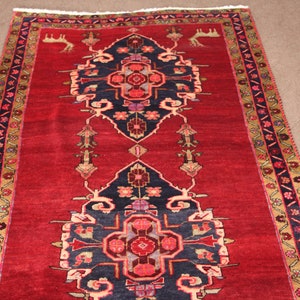 K&ouml;nnte beinhalten: Ein roter Teppich mit traditionellem persischem Design. Der Teppich hat ein zentrales Medaillon mit einem geometrischen Muster und einen Rand mit floralen Motiven.