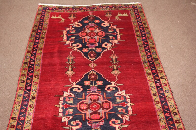 K&ouml;nnte beinhalten: Ein roter Teppich mit traditionellem persischem Design. Der Teppich hat ein zentrales Medaillon mit einem geometrischen Muster und einen Rand mit floralen Motiven.