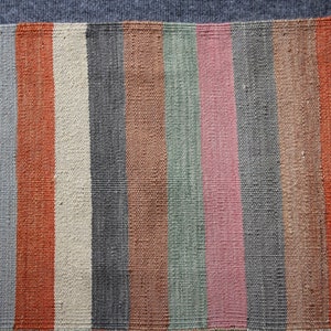 May include: A striped woven rug with a fringe on one side. The rug has alternating stripes of gray, orange, beige, brown, green, pink, and blue.