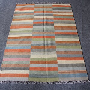 May include: A rectangular rug with a striped pattern in shades of orange, blue, green, and brown. The rug has a fringe border.
