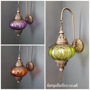 May include: Three wall sconces with ornate metal frames and glass globes. The globes are in purple, green, and amber colours. The sconces are mounted on a grey wall.