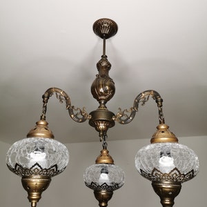 May include: A three-light chandelier with a gold finish and clear glass shades. The shades have a textured, crackled glass design.