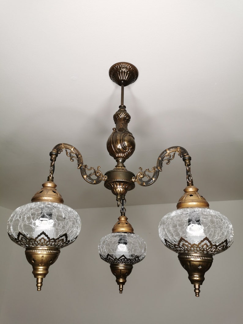 May include: A three-light chandelier with a gold finish and clear glass shades. The shades have a textured, crackled glass design.