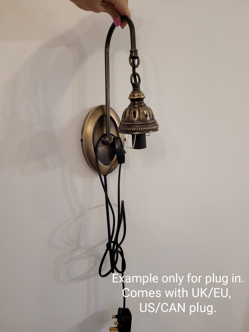 May include: A brass wall sconce with a decorative bell-shaped shade and a black cord. The sconce has a UK/EU plug, but comes with a US/CAN plug.