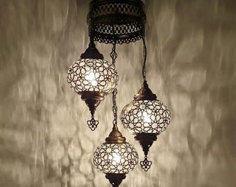 May include: A three-light chandelier with round, white glass shades featuring intricate geometric patterns. The shades are suspended from a metal frame with a decorative design.