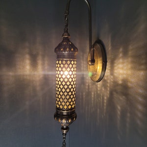 May include: A brass wall sconce with a decorative, patterned glass shade. The sconce has a traditional design and is lit with a warm, white light.