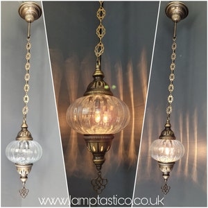May include: A vintage pendant light featuring a clear, ribbed glass shade and decorative brass-toned metalwork. The light hangs from a chain with ornate links and a ceiling fitting. The website address www.lamptastico.co.uk is visible.