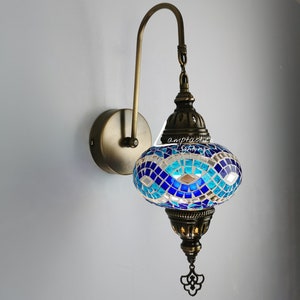 May include: A blue and white mosaic glass wall sconce with a brass finish. The sconce has a curved arm and a chain hanging from the top. The light bulb is not included.