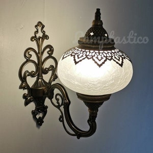 May include: A white frosted glass globe light fixture with an ornate brass wall mount. The globe has a decorative cut-out design around the top edge.