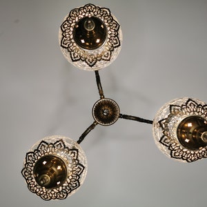 May include: A three-light chandelier with clear glass globes and intricate metalwork. Each globe has a decorative metal design and a gold-toned finish.