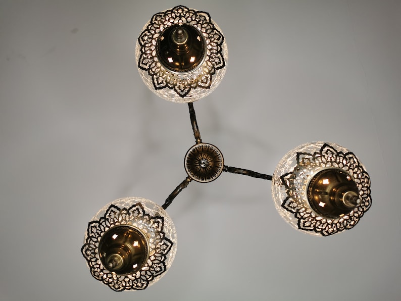 May include: A three-light chandelier with clear glass globes and intricate metalwork. Each globe has a decorative metal design and a gold-toned finish.