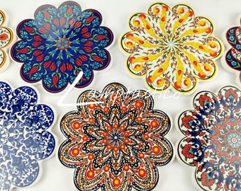 May include: A collection of ceramic coasters with a floral design. The coasters feature a scalloped edge and are decorated with intricate patterns in various colors, including blue, red, yellow, and orange. The coasters are arranged on a white surface.