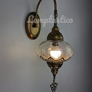 May include: A brass wall sconce with a clear glass globe shade featuring a crackled glass design. The sconce has a curved arm and a decorative metal finial.