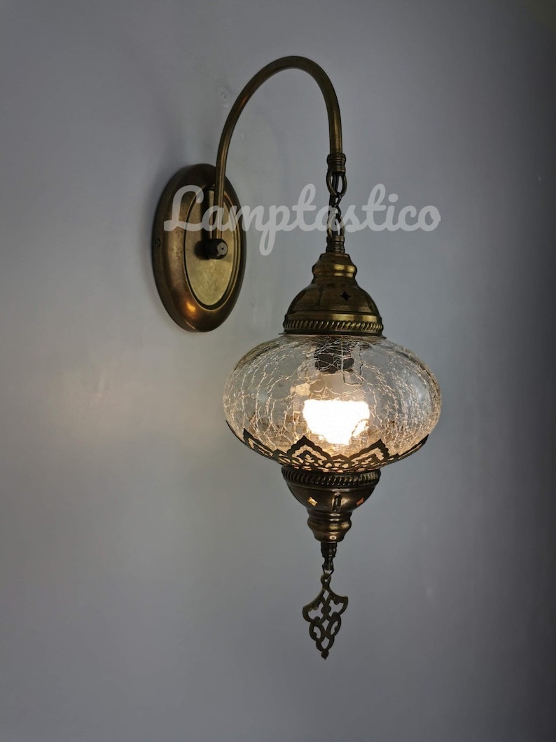May include: A brass wall sconce with a clear glass globe shade featuring a crackled glass design. The sconce has a curved arm and a decorative metal finial.