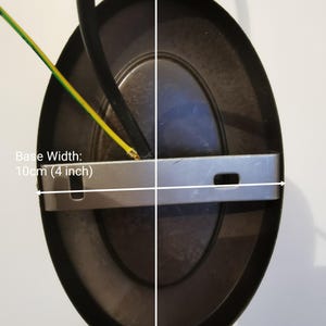 May include: A black metal ceiling light fixture with a round, oval-shaped base. The base measures 4 inches wide and 6 inches high. The fixture has a silver metal mounting plate and two wires.