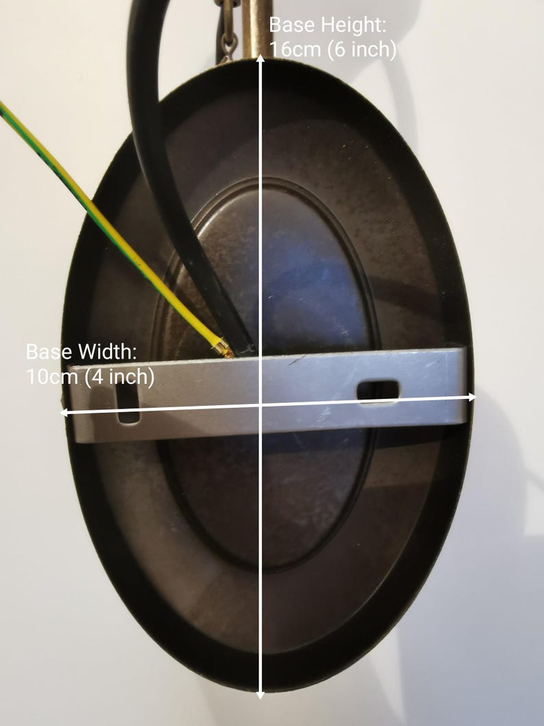 May include: A black metal ceiling light fixture with a round, oval-shaped base. The base measures 4 inches wide and 6 inches high. The fixture has a silver metal mounting plate and two wires.