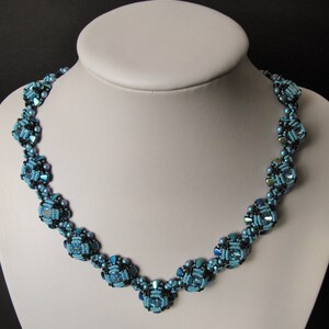 Könnte beinhalten: Eine blaue und schwarze Perlenkette mit geometrischem Design. Die Kette ist aus kleinen, facettierten Perlen gefertigt, die einen schimmernden Effekt erzeugen.