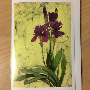 May include: Greeting card featuring a watercolor painting of purple iris flowers with green leaves against a yellow background. The card is in a clear plastic sleeve, with a white border.