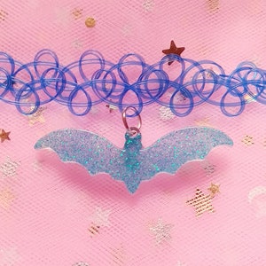 Op de afbeelding: Een blauwe plastic choker ketting met een lichtblauwe glitter vleermuis bedel.