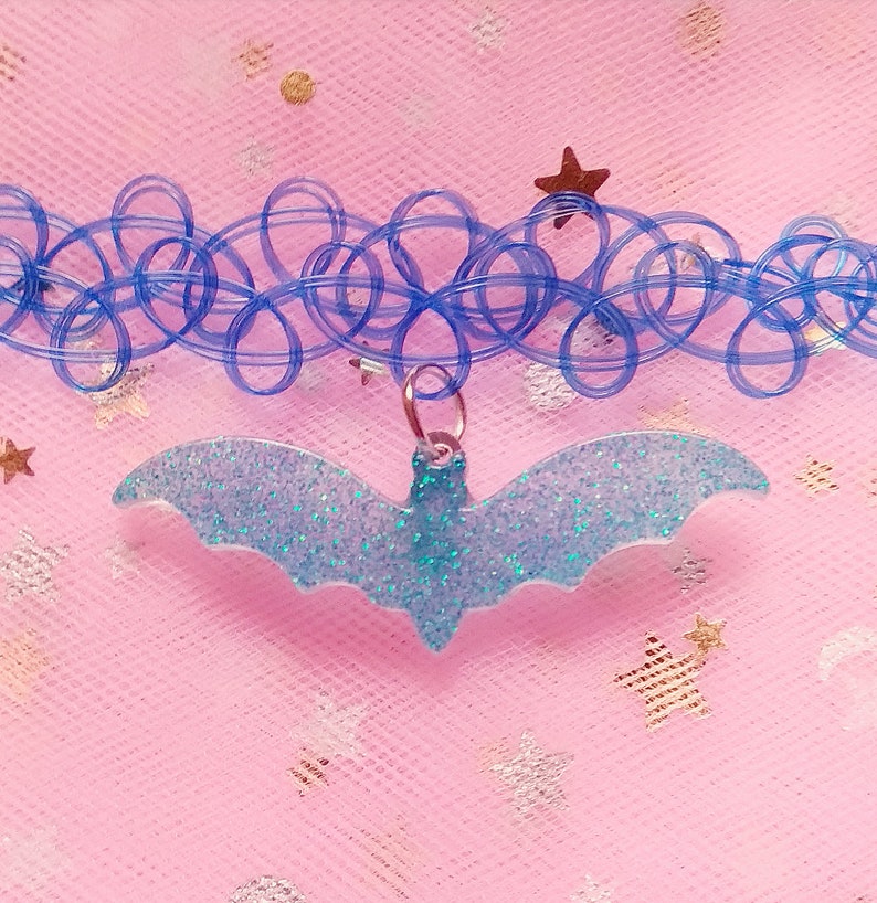 Op de afbeelding: Een blauwe plastic choker ketting met een lichtblauwe glitter vleermuis bedel.