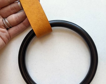 May include: A black wooden ring with a mustard yellow leather strap. The strap has a screw in the centre.