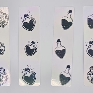 Puede incluir: Juego de ocho marcapáginas blancos con ilustraciones negras de botellas de pociones. Algunas botellas tienen forma de corazón, otras tienen un diseño de serpiente y calavera. Las ilustraciones están delineadas en negro, con un brillo holográfico.