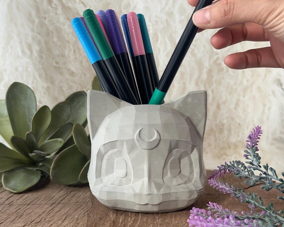 A geometric cat-shaped concrete planter/candle holder — the lunar cat silhouette is visually striking and the handmade cement texture gives it real tactile presence.