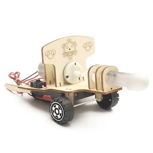 Könnte beinhalten: Ein Holzspielzeugauto mit einer Spritze, die hinten angebracht ist. Das Auto hat einen schwarzen Motor und schwarze Räder. Das Auto hat ein Holzschild hinten mit einem Comic-Gesicht und den Worten "ER USE".