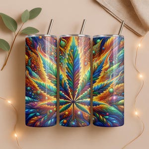 Op de afbeelding: Drie roestvrijstalen bekers met een kleurrijk cannabisbladontwerp. Het ontwerp heeft een levendige mix van blauw, groen, geel en oranje. Elke beker heeft een zilveren rietje en een bijpassende deksel. De bekers zijn ongeveer 23 cm hoog.