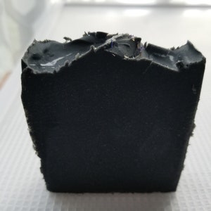 Puede incluir: Una barra de jabón negra con una textura rugosa. El jabón tiene un ligero tono púrpura.