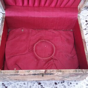 May include: An antique wooden box with a red velvet lining and a circular indentation in the center. The box is painted with a marbled pattern.